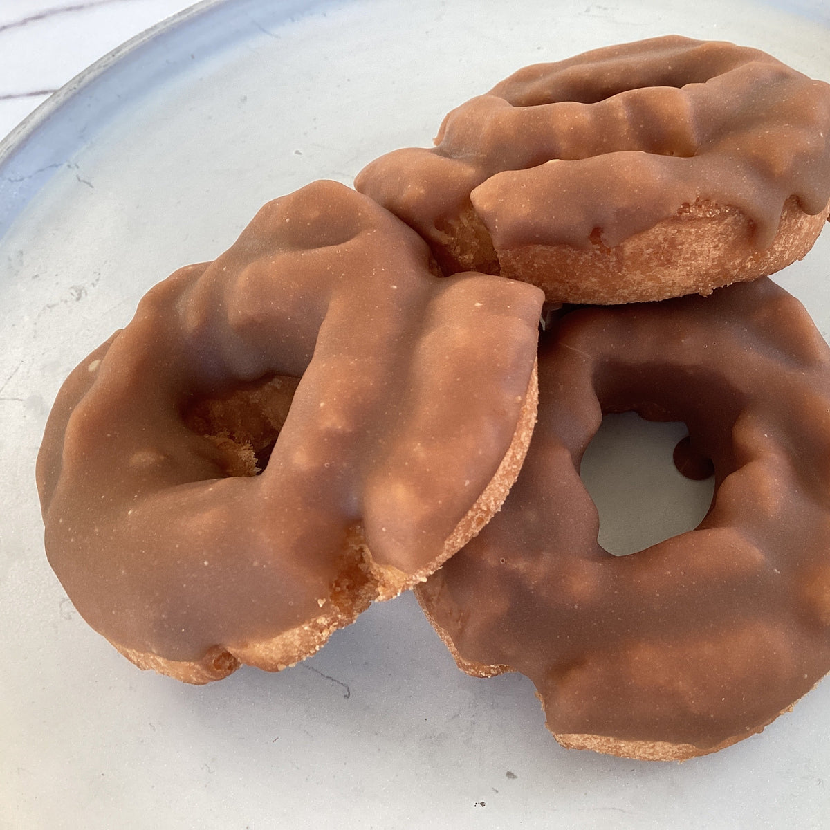 Three maple-glazed donuts stacked on a white plate